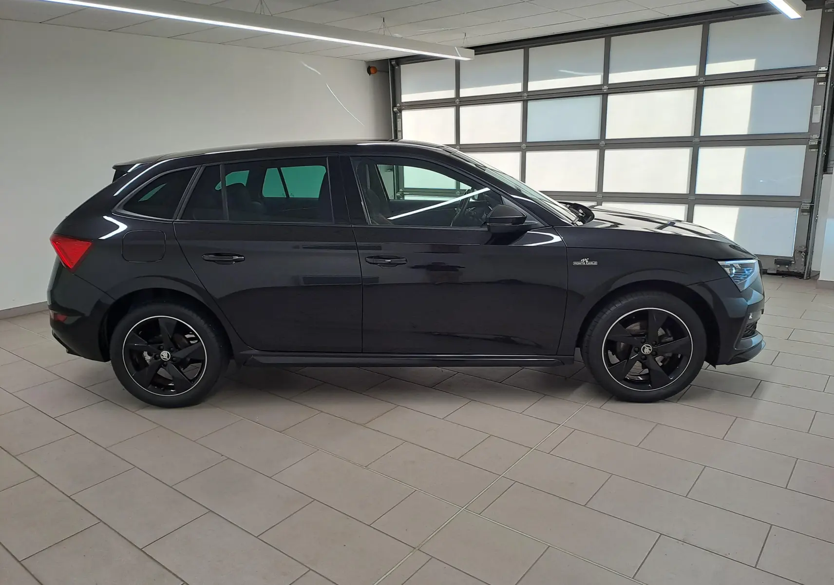 Profil côté gauche d'une Skoda Scala 1.0 TSI Monte-Carlo noire nacrée avec jantes noires en intérieur clair.