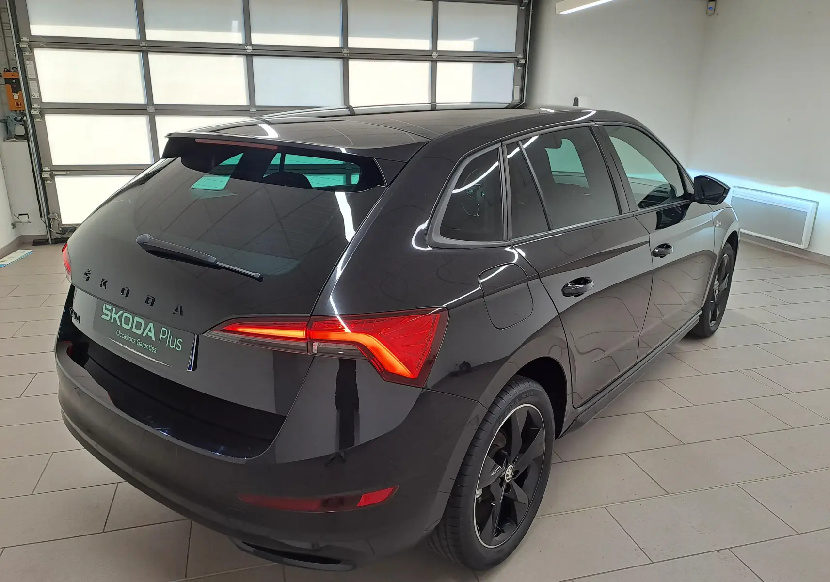 Vue 3/4 arrière droite d'une Skoda Scala 2022 noire nacrée avec jantes noires et feux arrière allumés dans un garage.