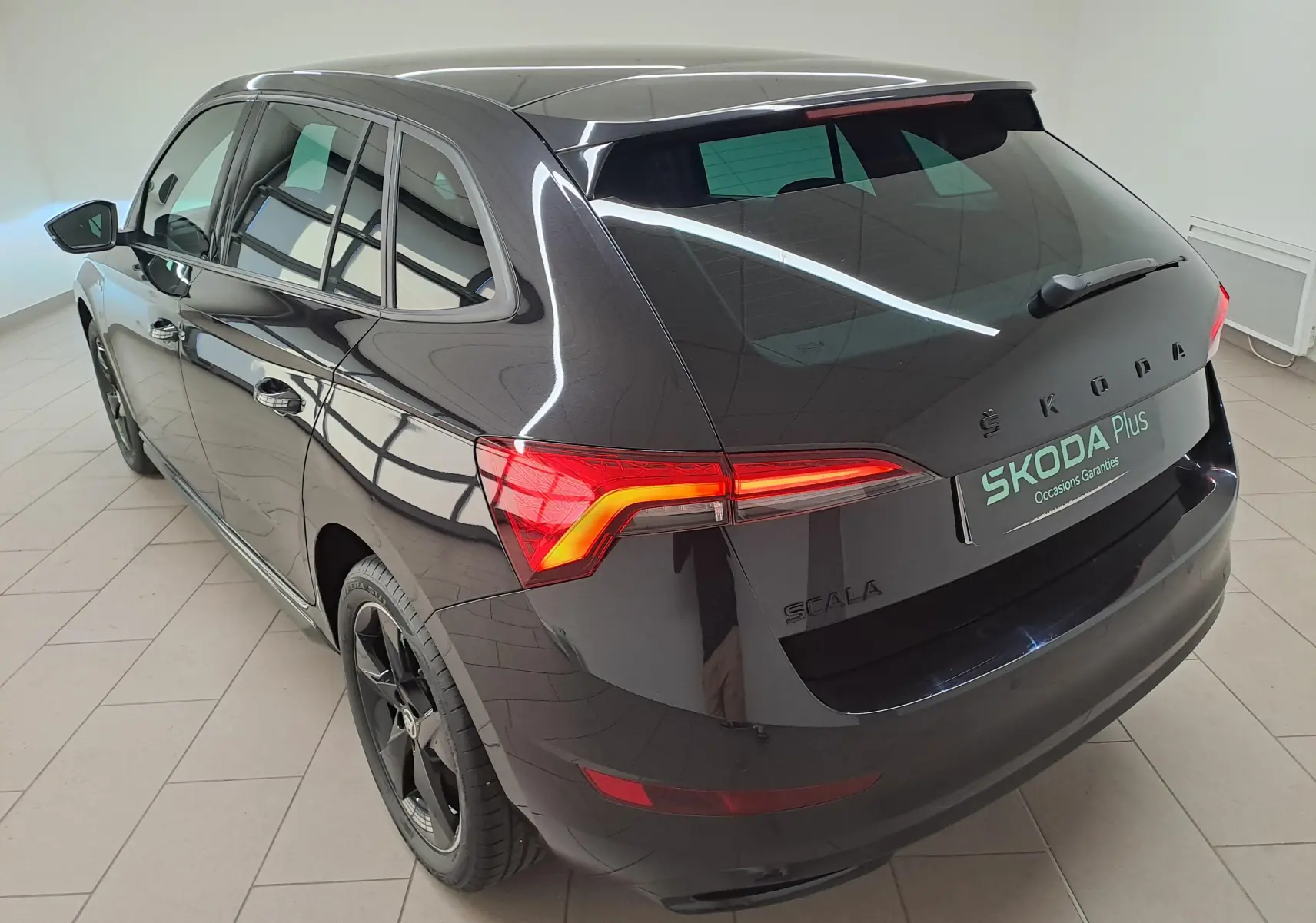 Vue 3/4 arrière gauche d'une Skoda Scala 2022 noire nacrée avec feux arrière allumés et jantes noires Monte-Carlo.