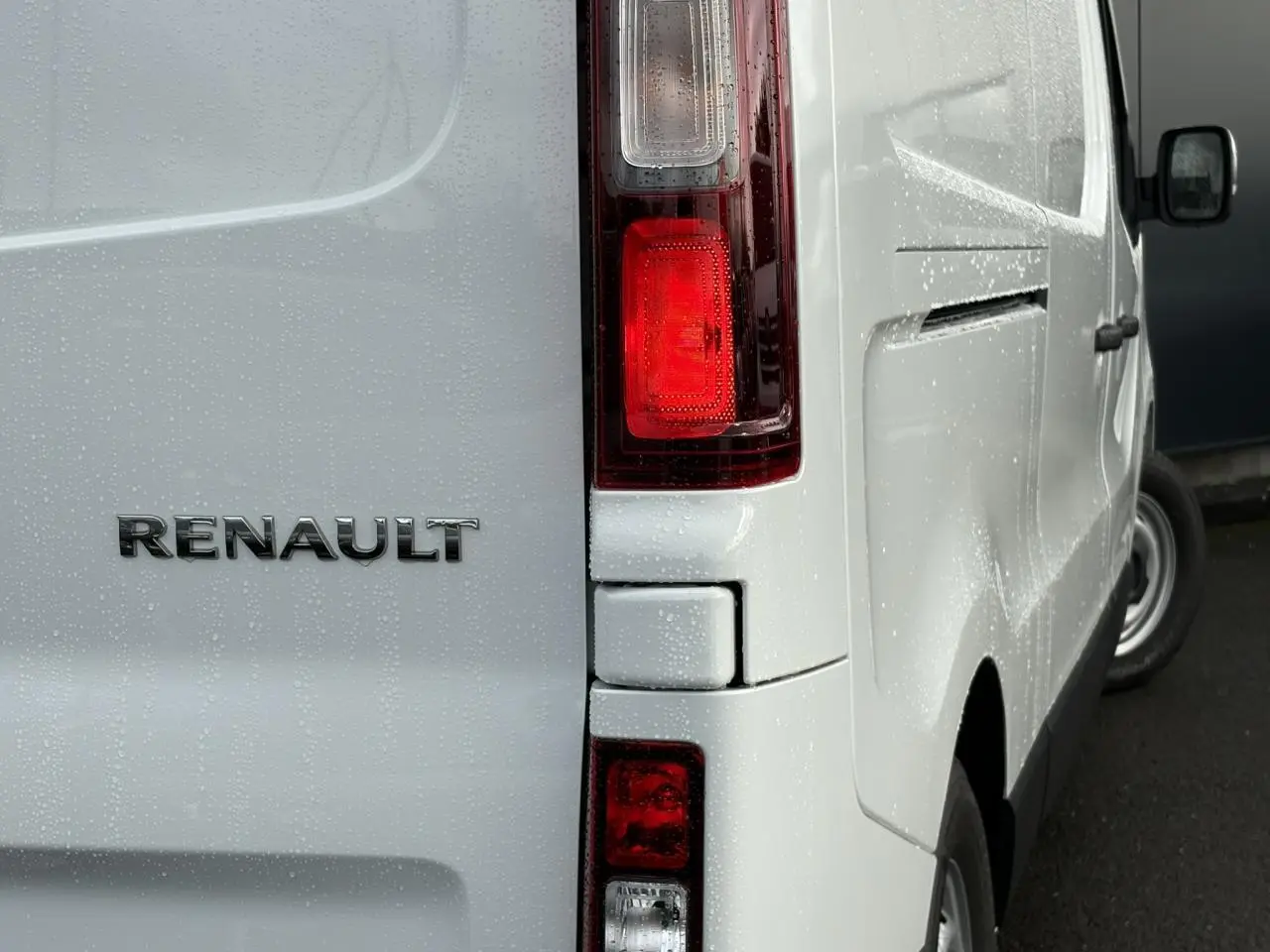 Détail arrière droit du Renault Trafic Fourgon blanc Glacier avec feux arrière et logo Renault sous la pluie.