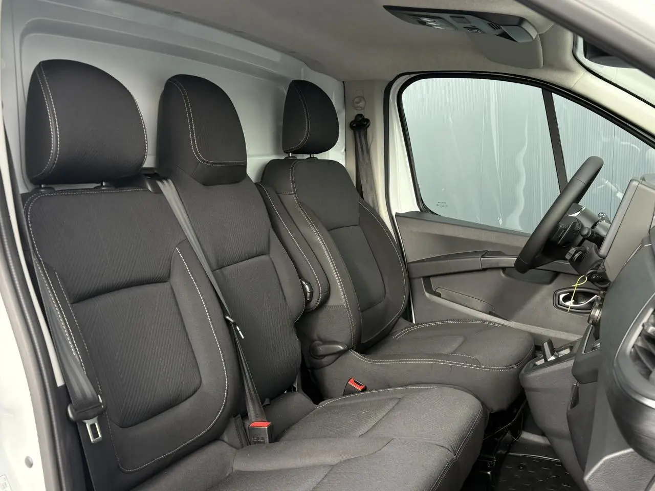 Vue intérieure côté conducteur du Renault Trafic Fourgon 2026, sièges tissu noir avec surpiqûres blanches.