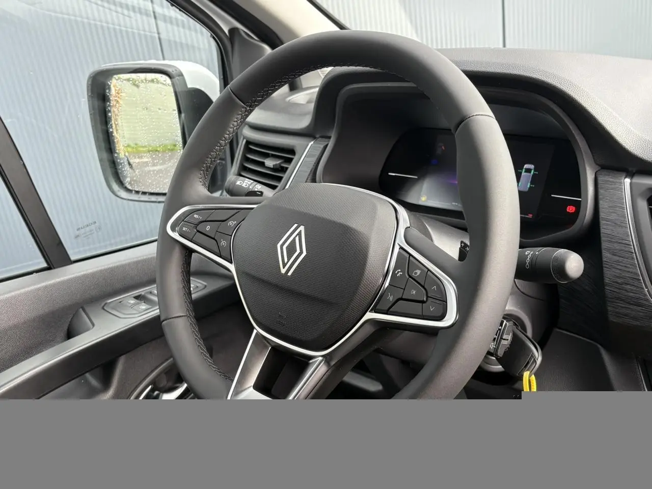 Vue intérieure rapprochée du volant multifonction Renault Trafic Fourgon, avec tableau de bord numérique et rétroviseur côté gauche.