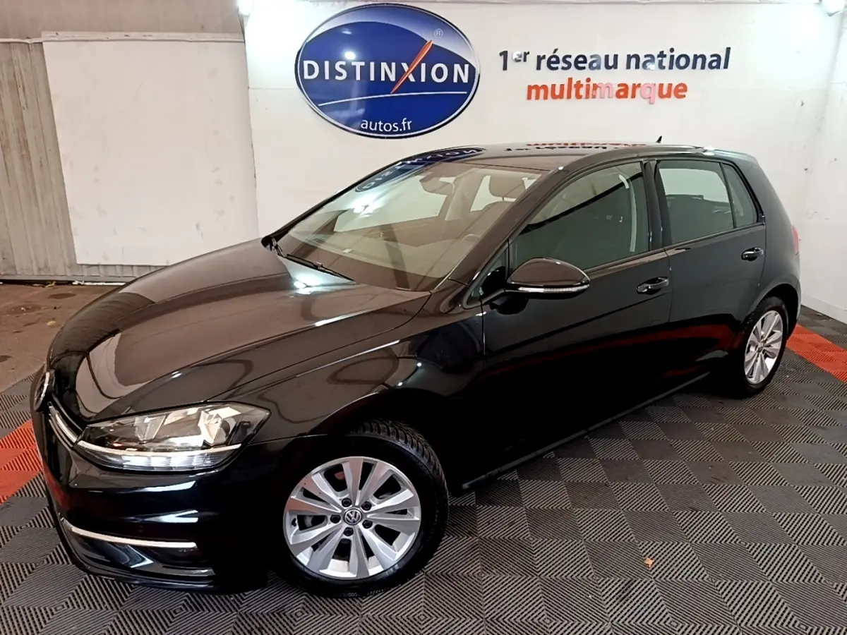 Volkswagen Golf noire vue en 3/4 avant droit, avec jantes argentées et phares allumés.