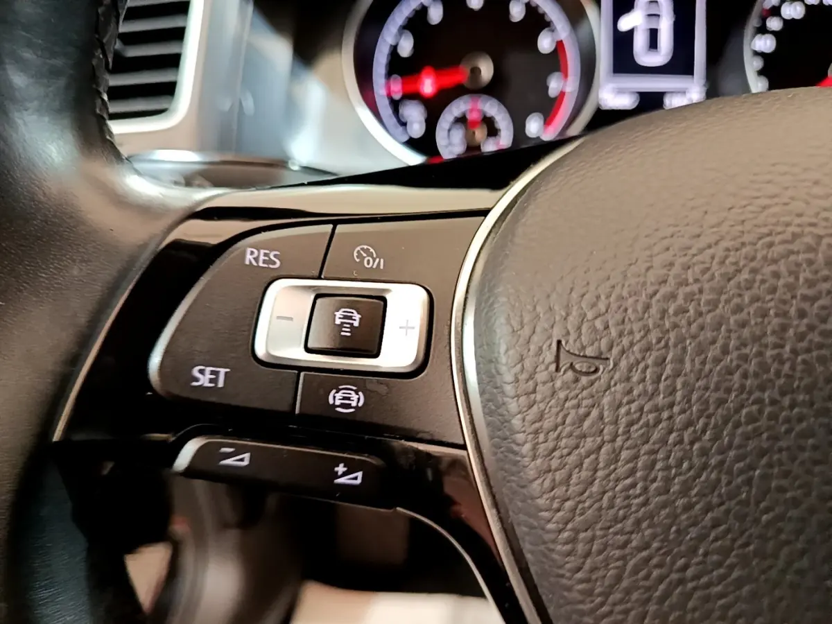 Gros plan sur le volant cuir noir de la Volkswagen Golf 2019, avec commandes multifonctions et tableau de bord flou.