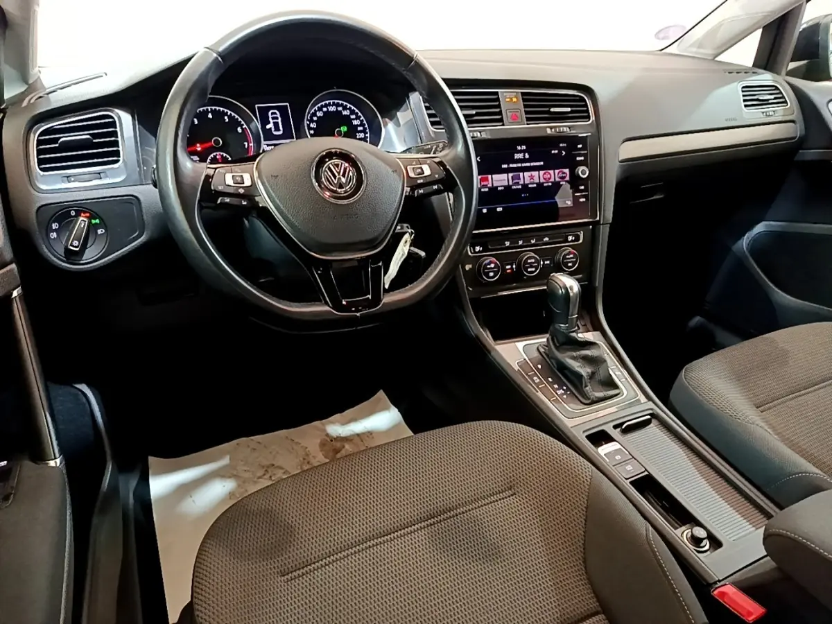 Vue intérieure centrée sur le volant cuir multifonctions et la console centrale d'une Volkswagen Golf noire de 2019.