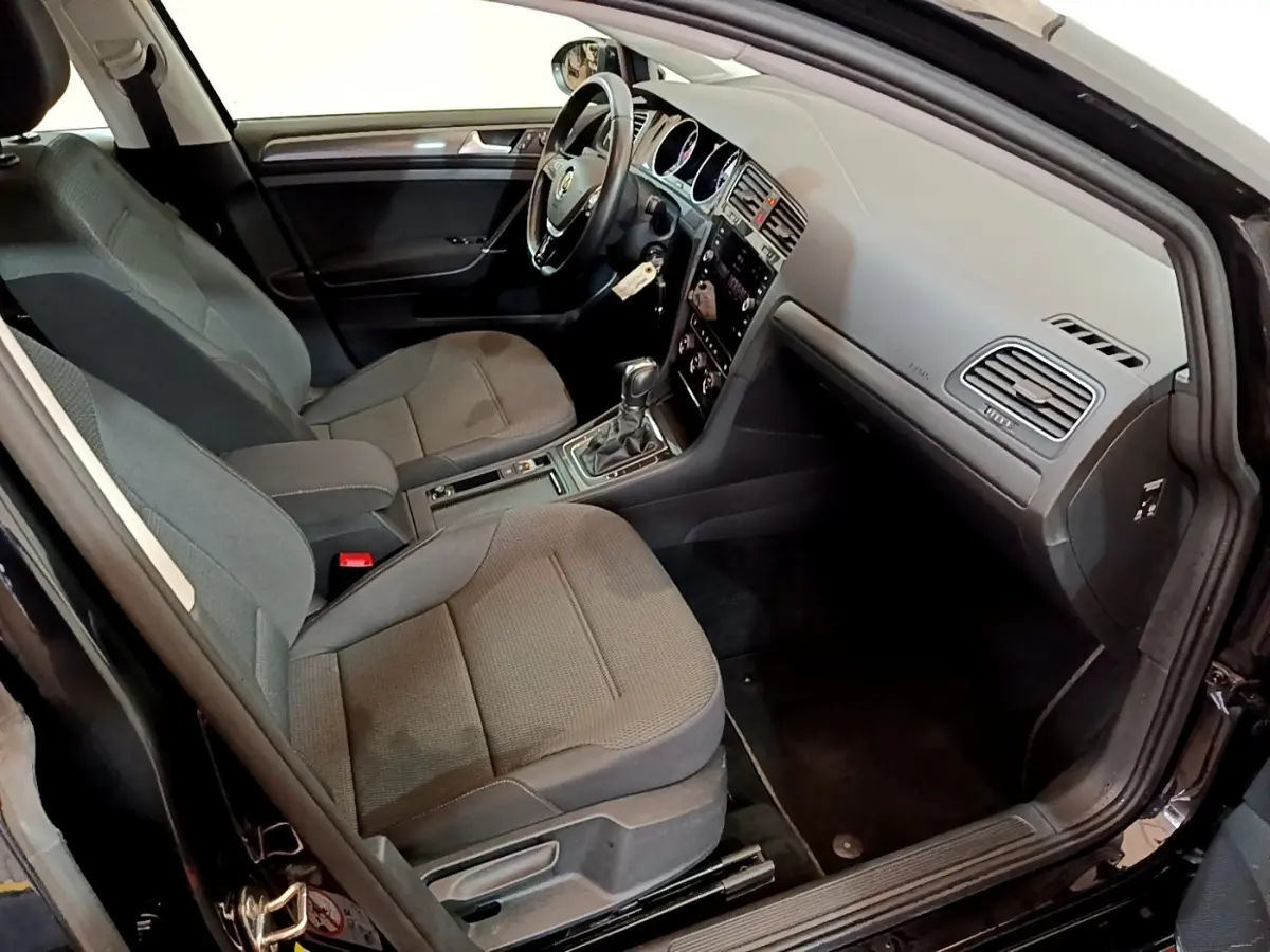 Vue intérieure côté conducteur d’une Volkswagen Golf noire de 2019 avec sièges tissu gris et volant cuir multifonctions.