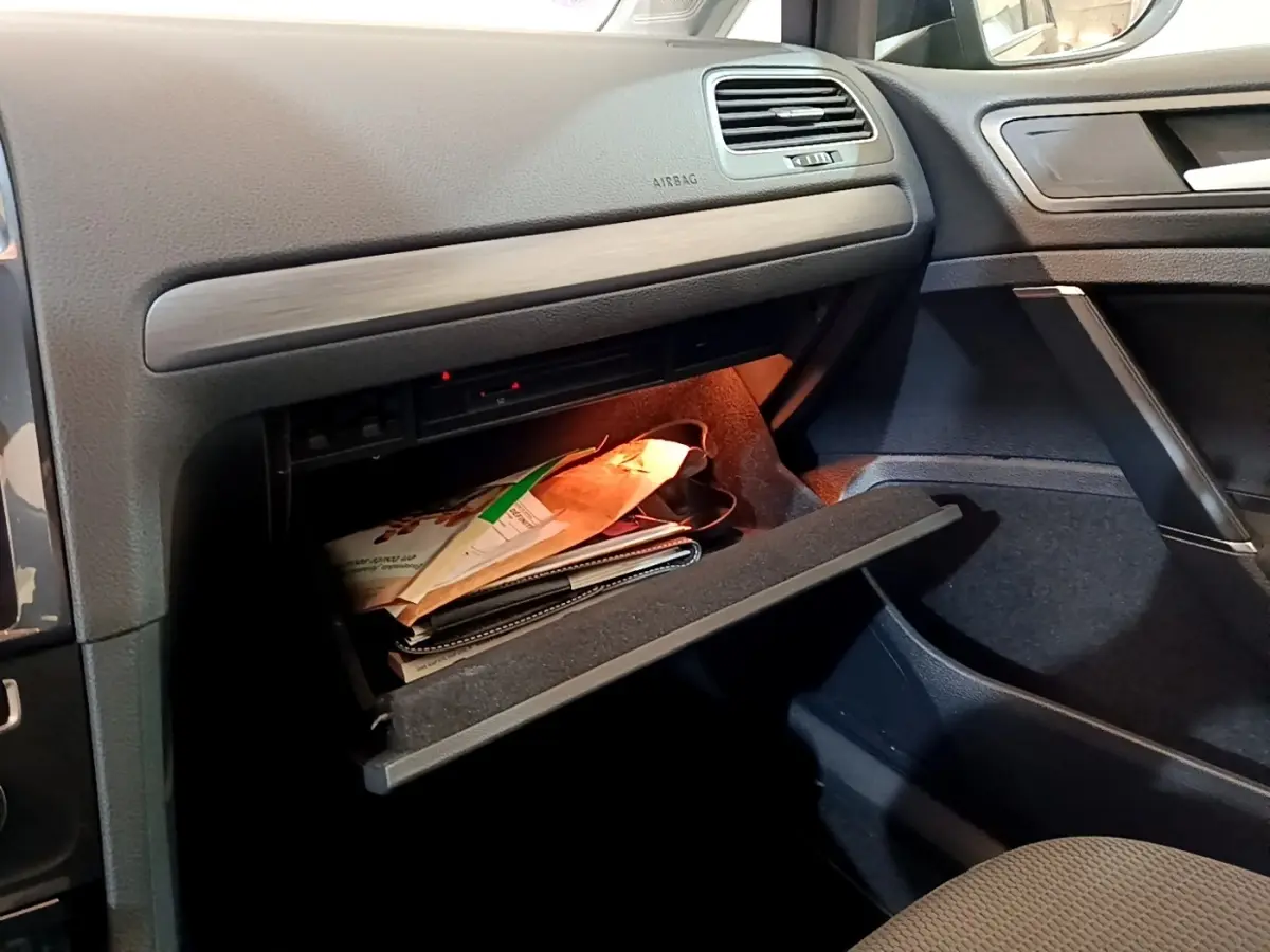 Vue intérieure côté passager d'une Volkswagen Golf noire de 2019, boîte auto, avec boîte à gants ouverte contenant des documents.