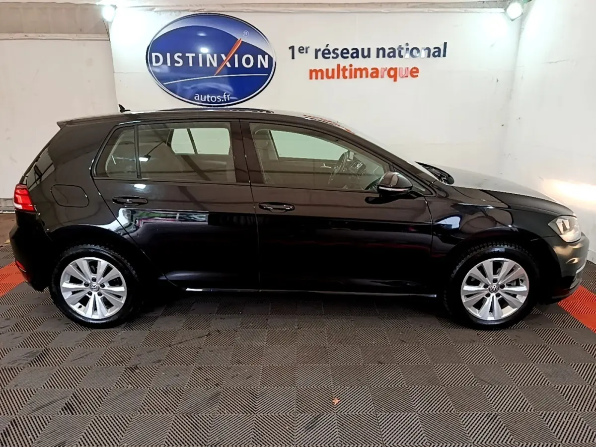 Profil droit d'une Volkswagen Golf noire 2019 stationnée en intérieur avec logo Distinxion en arrière-plan.