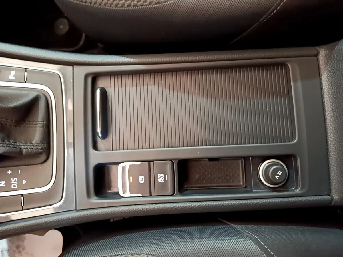 Vue rapprochée de la console centrale noire de la Volkswagen Golf 1.0 TSI 115 DSG7 avec frein à main électrique et prise 12V.