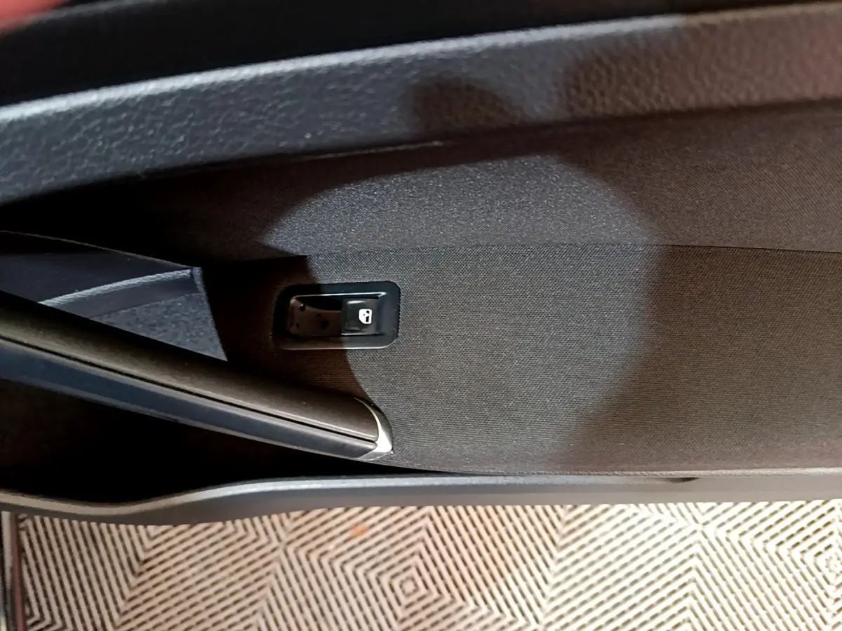 Détail de la commande d'ouverture de coffre intégrée dans le revêtement intérieur noir de la porte arrière droite d'une Volkswagen Golf noire.