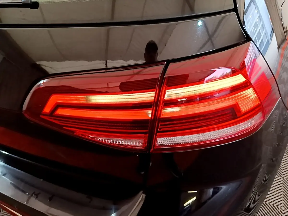 Gros plan sur le feu arrière droit allumé d’une Volkswagen Golf noire, reflétant l’environnement intérieur.