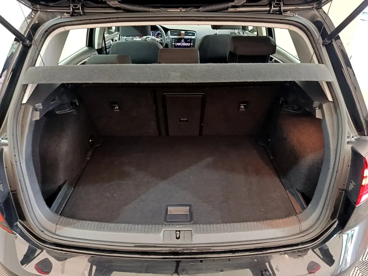 Coffre ouvert d’une Volkswagen Golf noire vue de l’arrière, montrant l’espace de chargement et la banquette arrière.