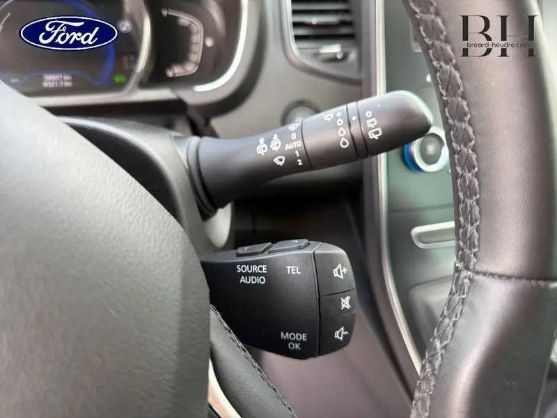 Le volant cuir noir et les commandes audio au volant d'un Renault Grand Scenic gris Cassiopée, vue rapprochée côté gauche.
