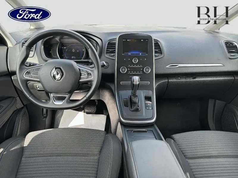 Vue intérieure avant du Renault Grand Scenic gris Cassiopée, montrant le volant cuir, écran tactile central et console de boîte auto.