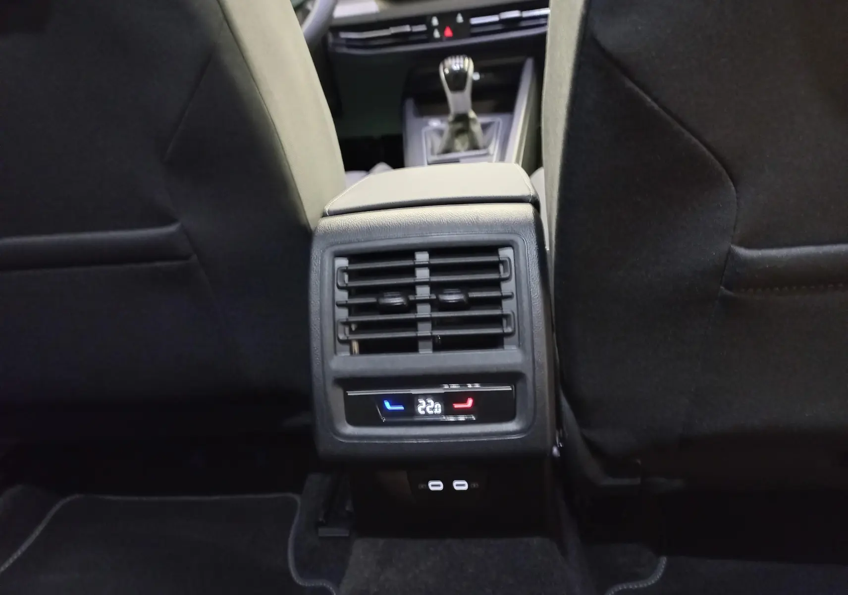Vue rapprochée de la console arrière entre les sièges avant d'une Volkswagen Golf Bleu Anemone avec commandes de climatisation et ports USB.