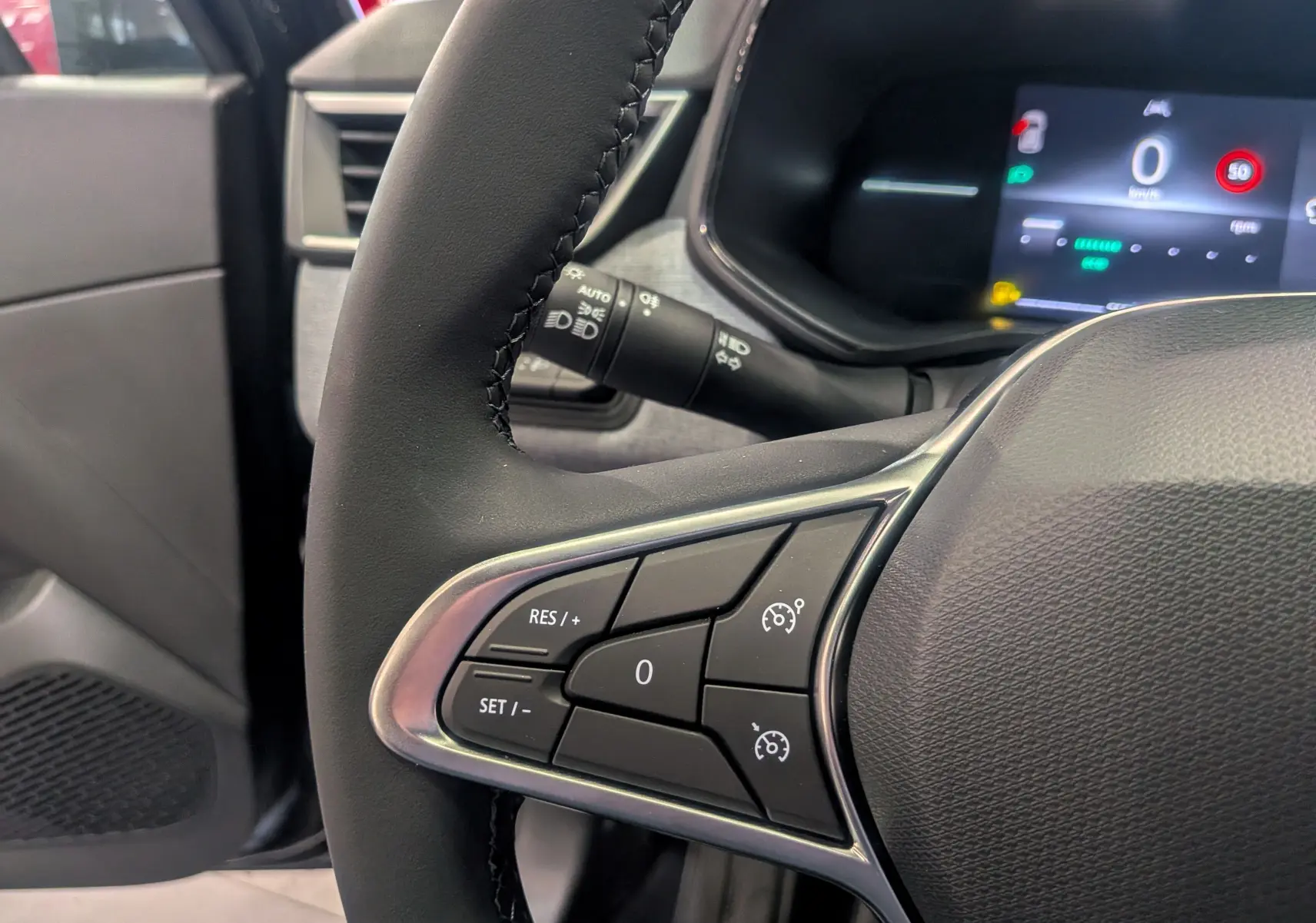 Gros plan sur le volant noir de la Renault Clio V 2025, avec commandes de régulateur de vitesse et tableau de bord digital en arrière-plan.