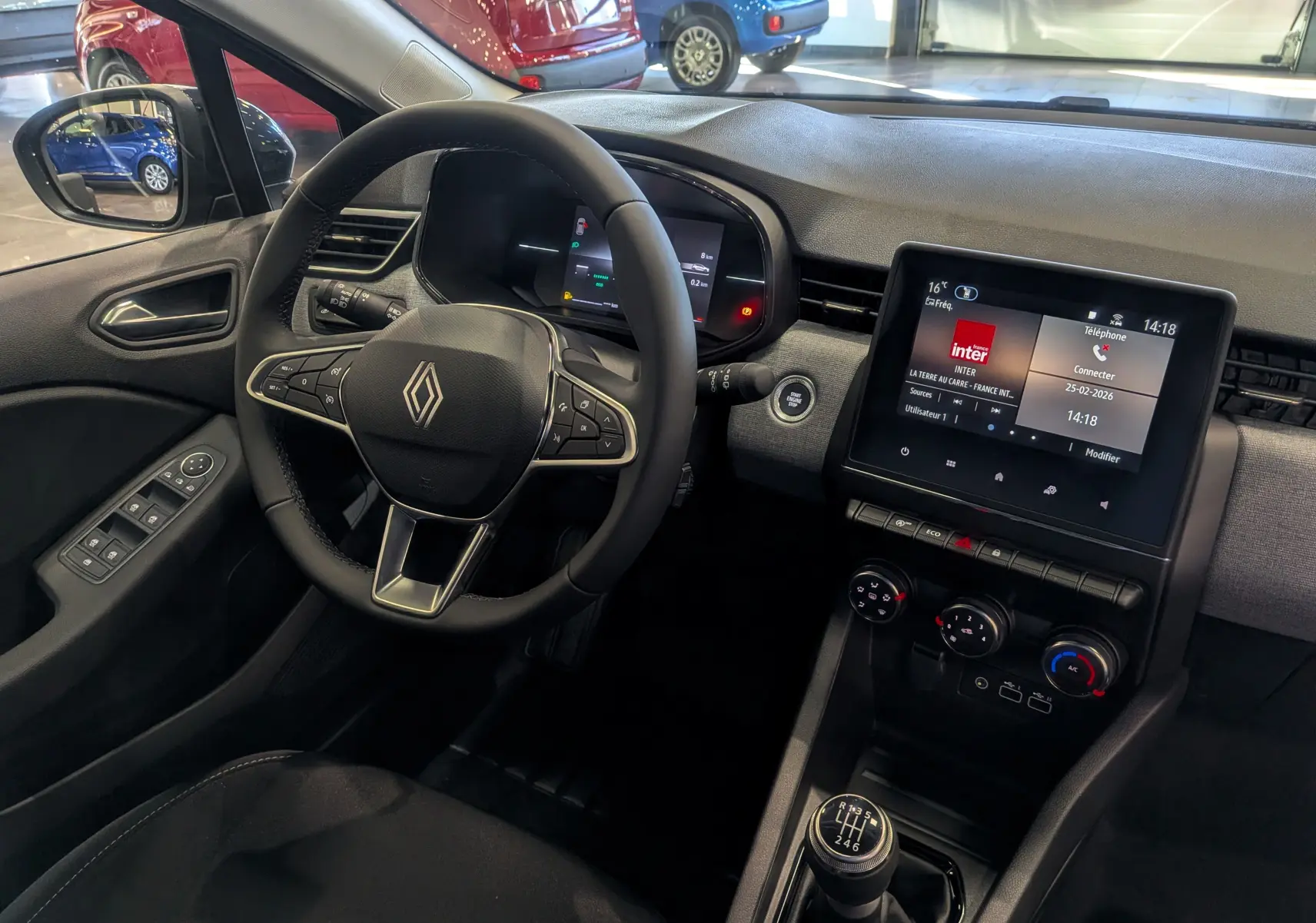 Vue intérieure côté conducteur de la Renault Clio V noire, avec volant multifonction, écran tactile et boîte manuelle six vitesses.