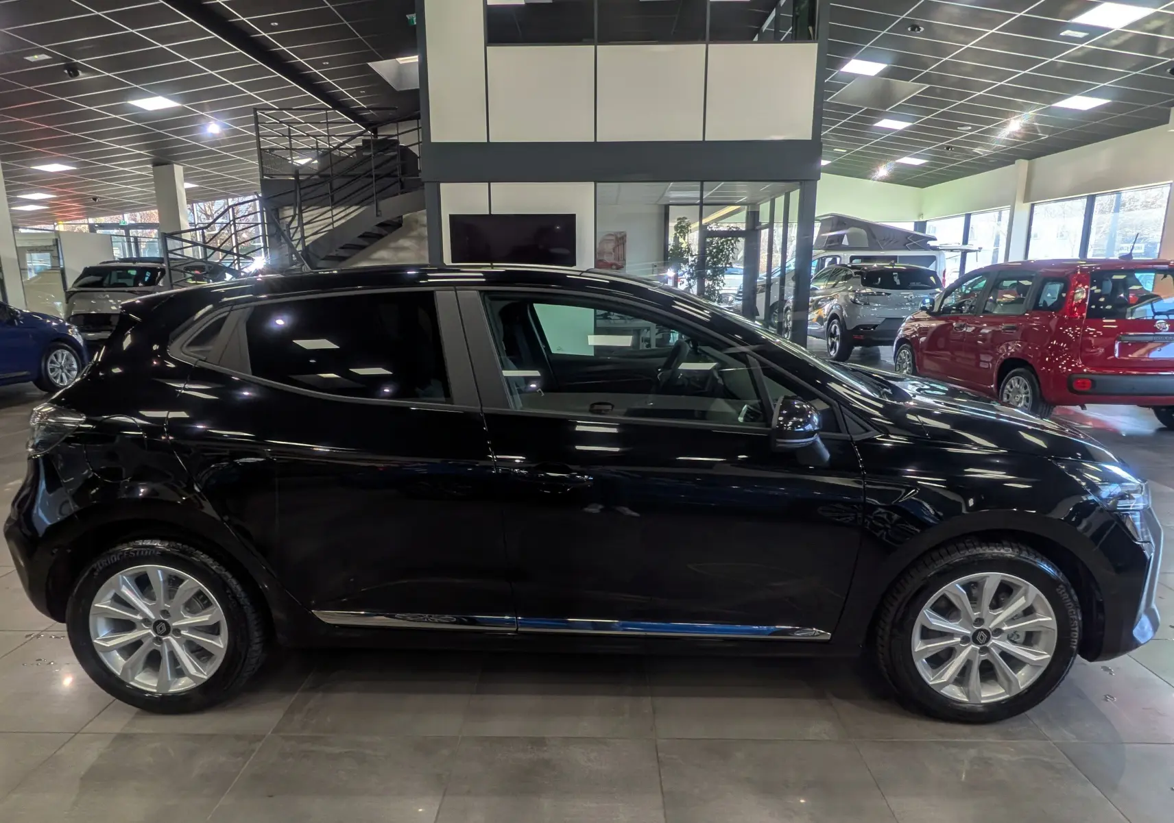 Profil côté gauche d'une Renault Clio V noire 2025 en intérieur, avec jantes alliage et vitres teintées.