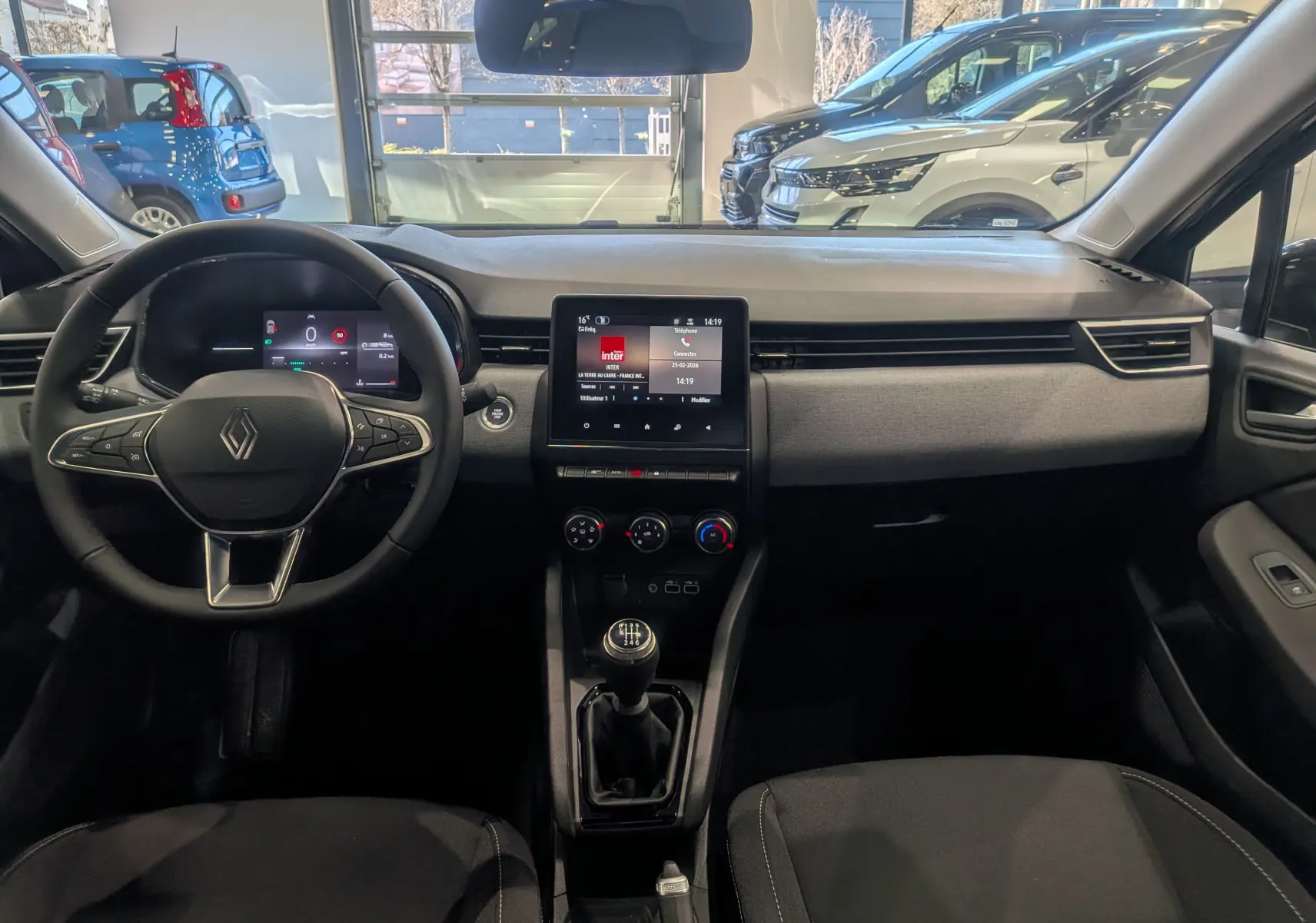 Vue intérieure avant de la Renault Clio V noire, mettant en valeur le tableau de bord moderne avec écran tactile et boîte manuelle.
