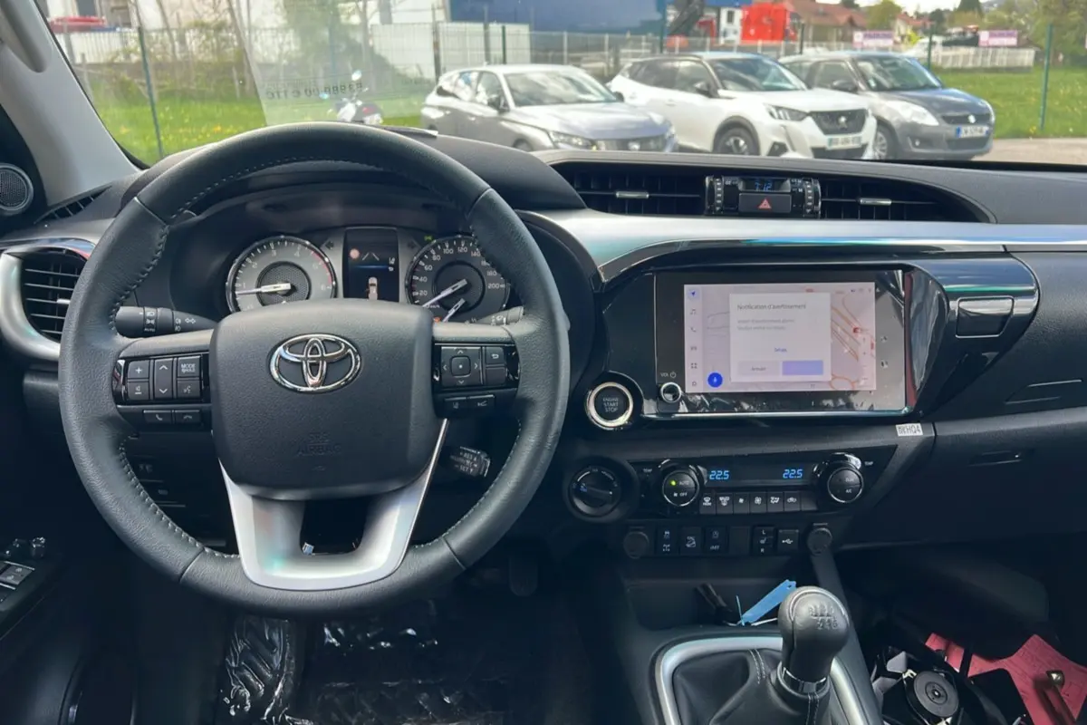Intérieur du Toyota Hilux 2025 vert métal, vue du poste de conduite avec volant, tableau de bord et levier de vitesse manuel.