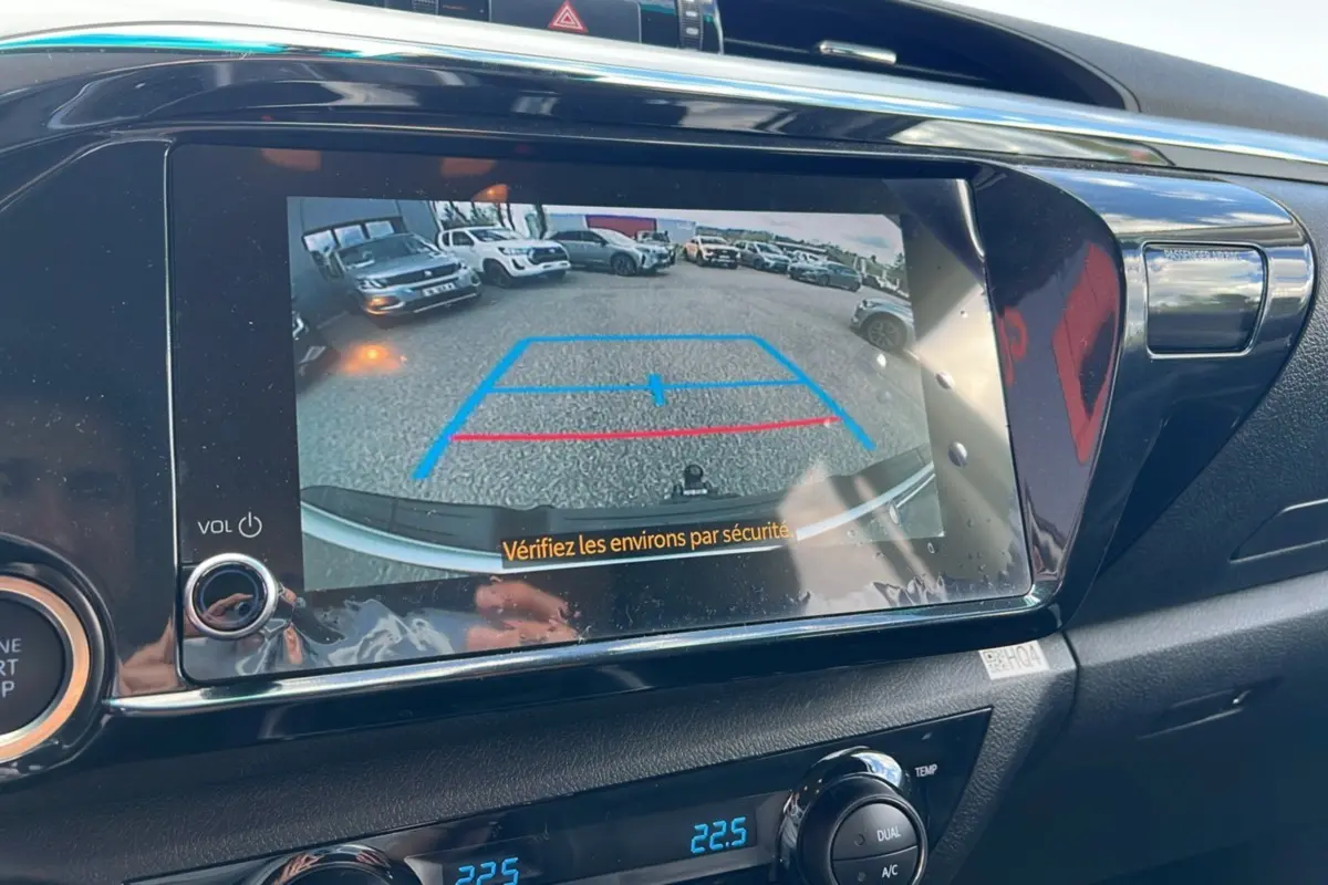 Vue arrière via caméra de recul du Toyota Hilux 4x4 vert métal 2025, avec lignes de guidage bleues et rouges à l'écran.