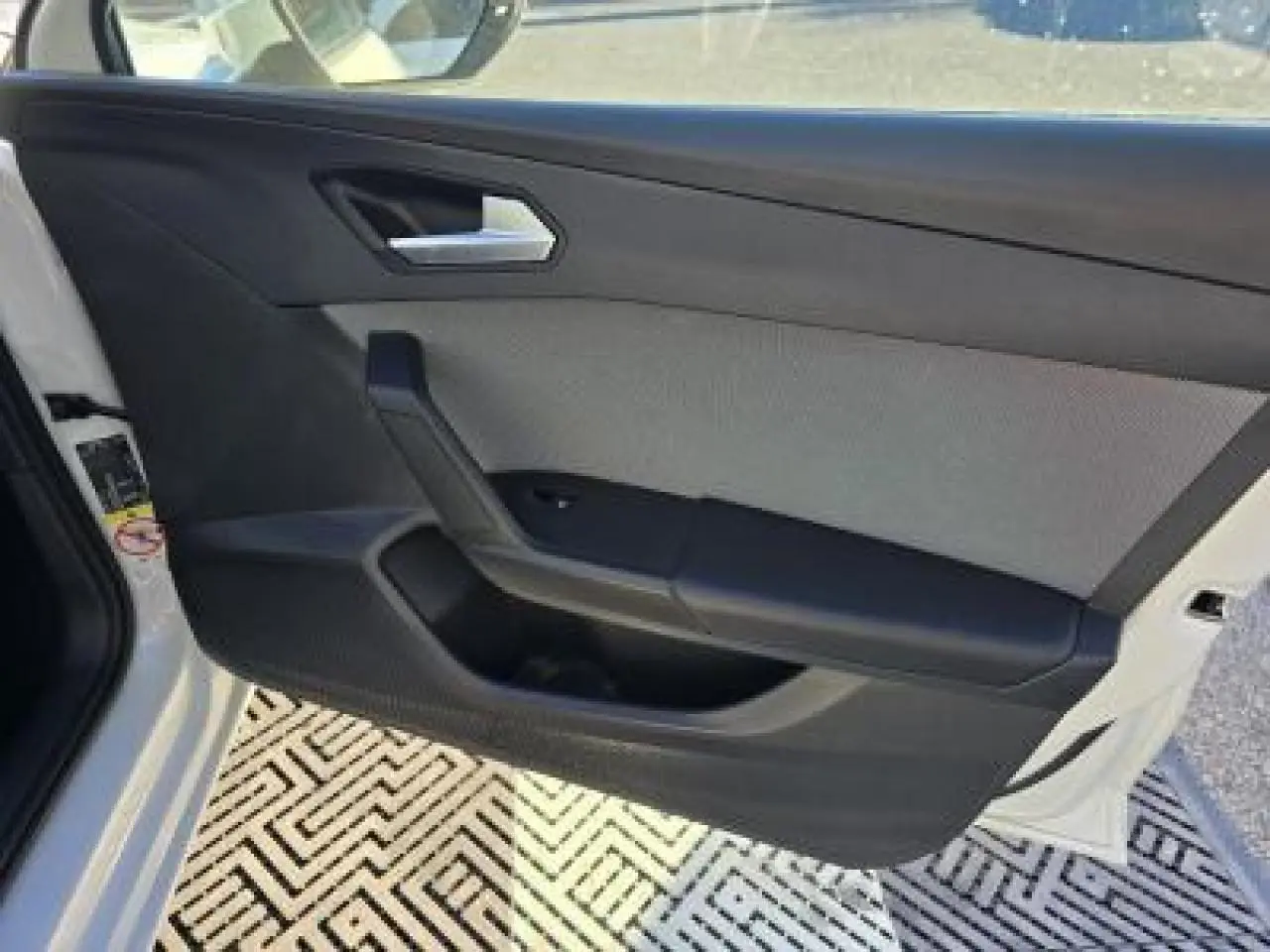 Porte avant gauche ouverte d'une SEAT LEON blanche, montrant le panneau intérieur noir et gris avec poignée argentée.