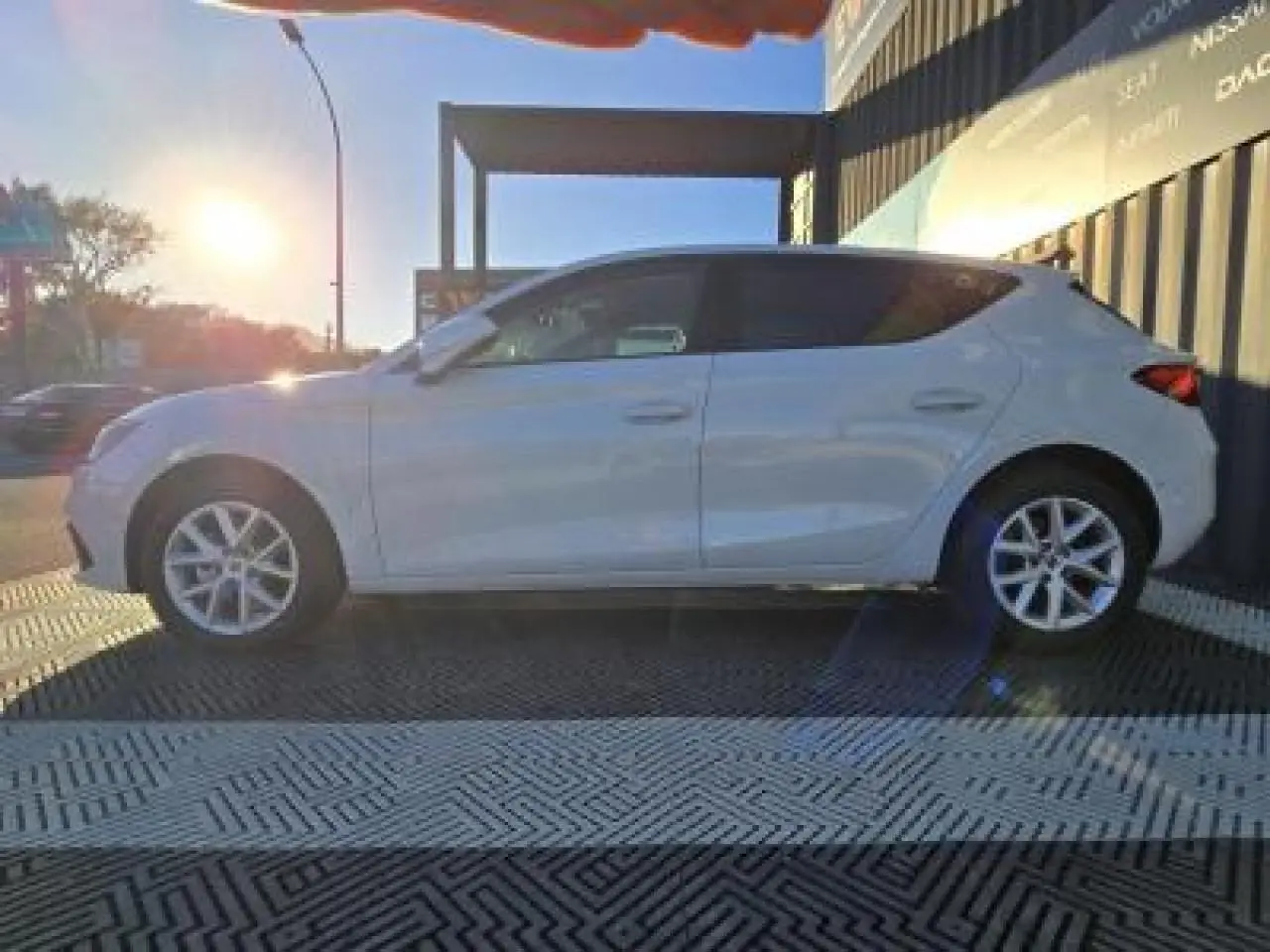 Profil côté gauche d'une SEAT LEON blanche 2024 stationnée, avec jantes alliage et arrière légèrement en ombre.