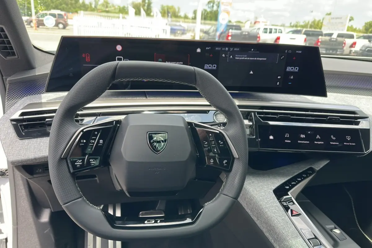Vue intérieure centrée sur le volant cuir multifonctions et les écrans digitaux du Peugeot 5008 Hybrid GT 2025.