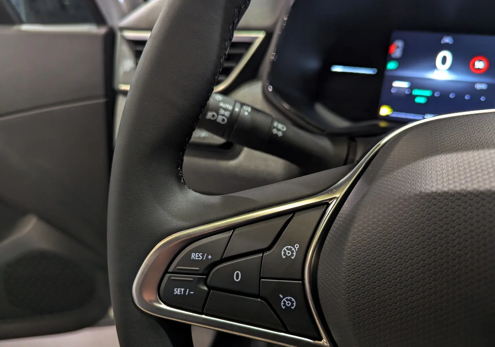 Gros plan sur les commandes au volant côté gauche du Renault Clio V 2025, intérieur noir avec écran numérique en arrière-plan.