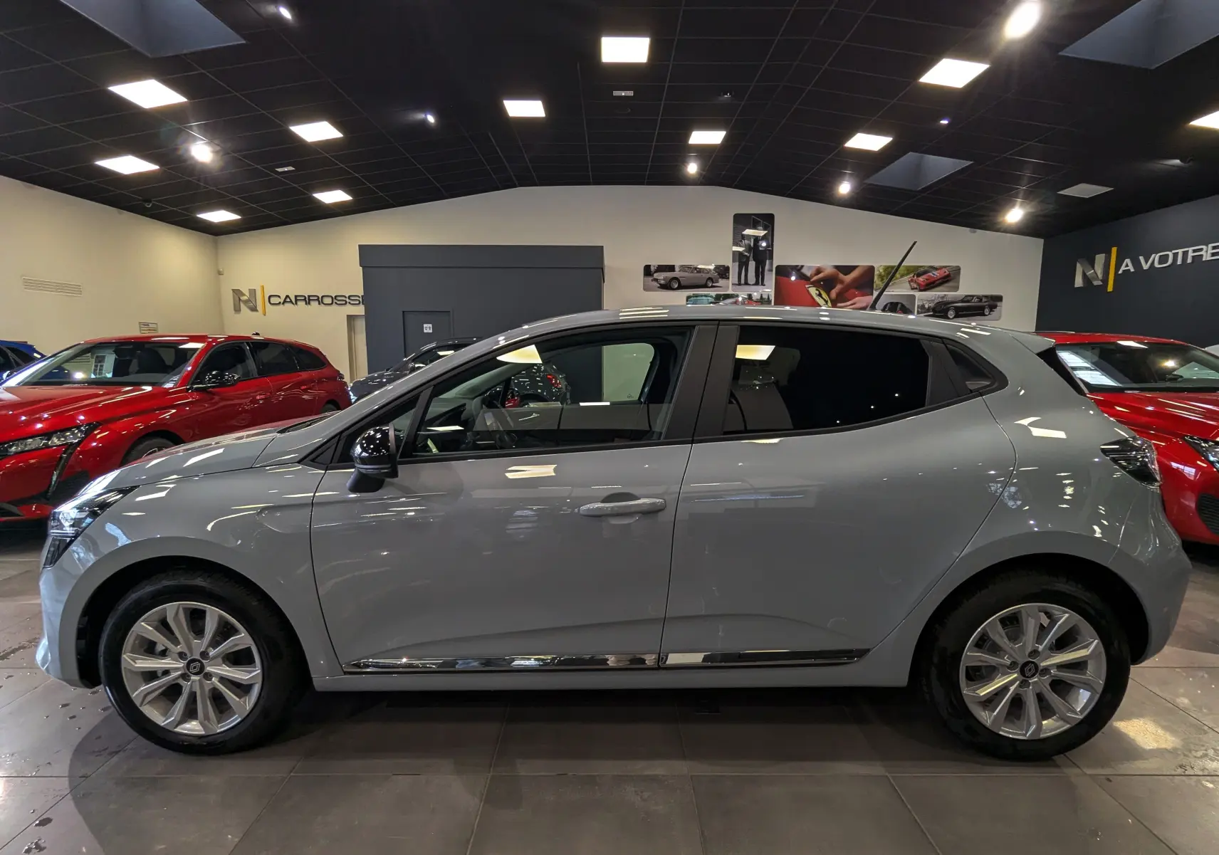 Profil côté gauche de la Renault Clio V gris Rafale en intérieur, avec jantes alliage et vitres teintées.