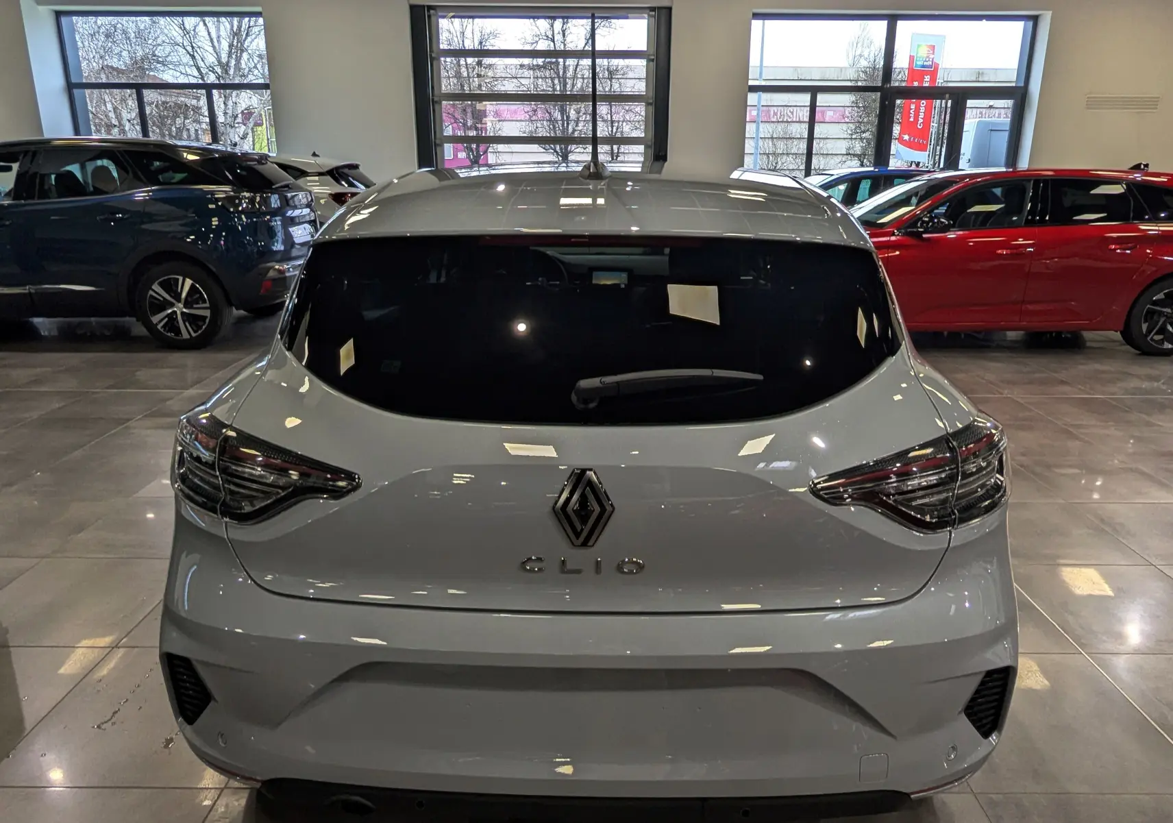 Vue arrière d'une Renault Clio V gris Rafale en intérieur, mettant en valeur ses feux et son logo central.