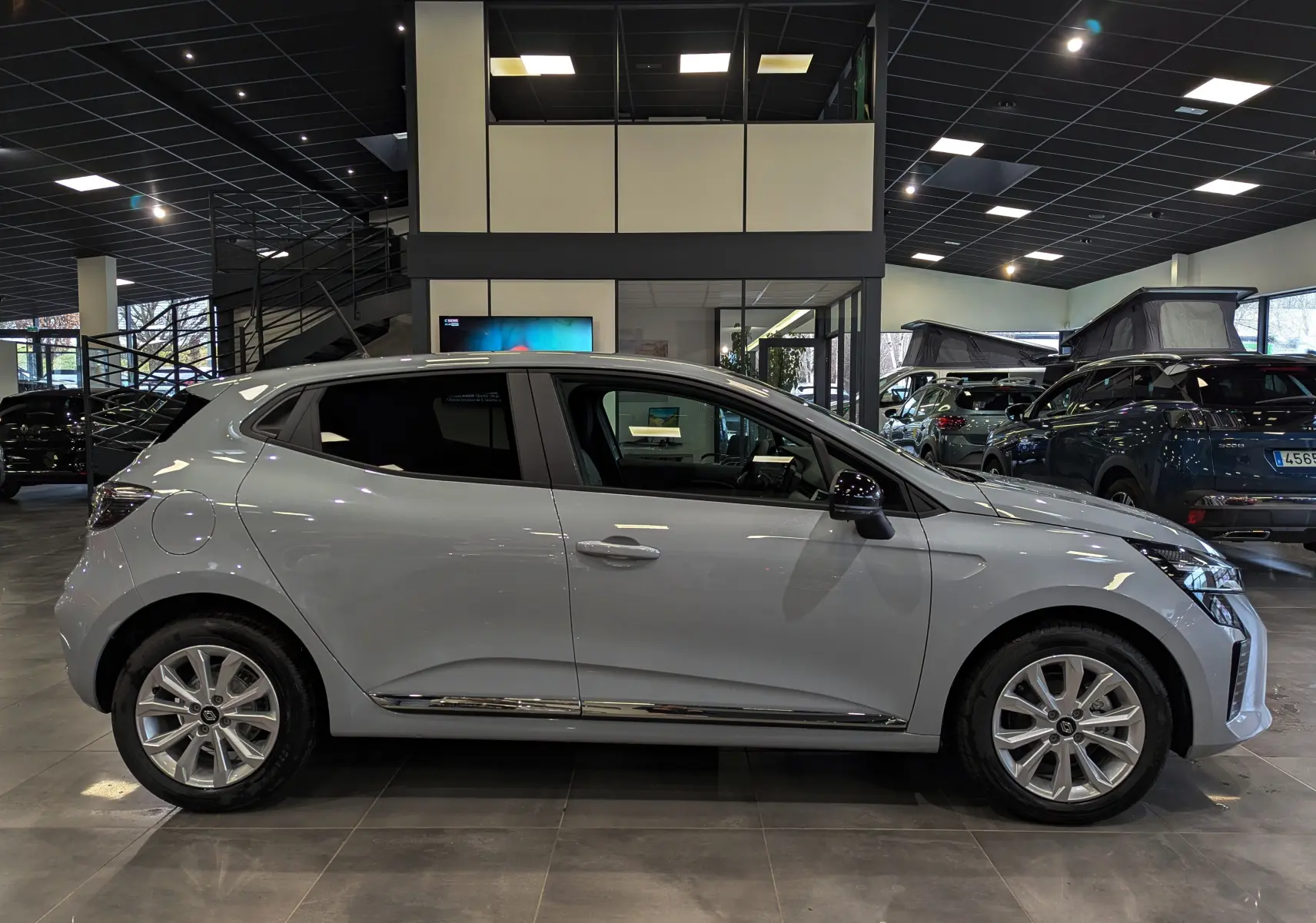 Profil côté gauche de la Renault Clio V gris Rafale 2025 en intérieur, avec jantes alliage et vitres teintées.