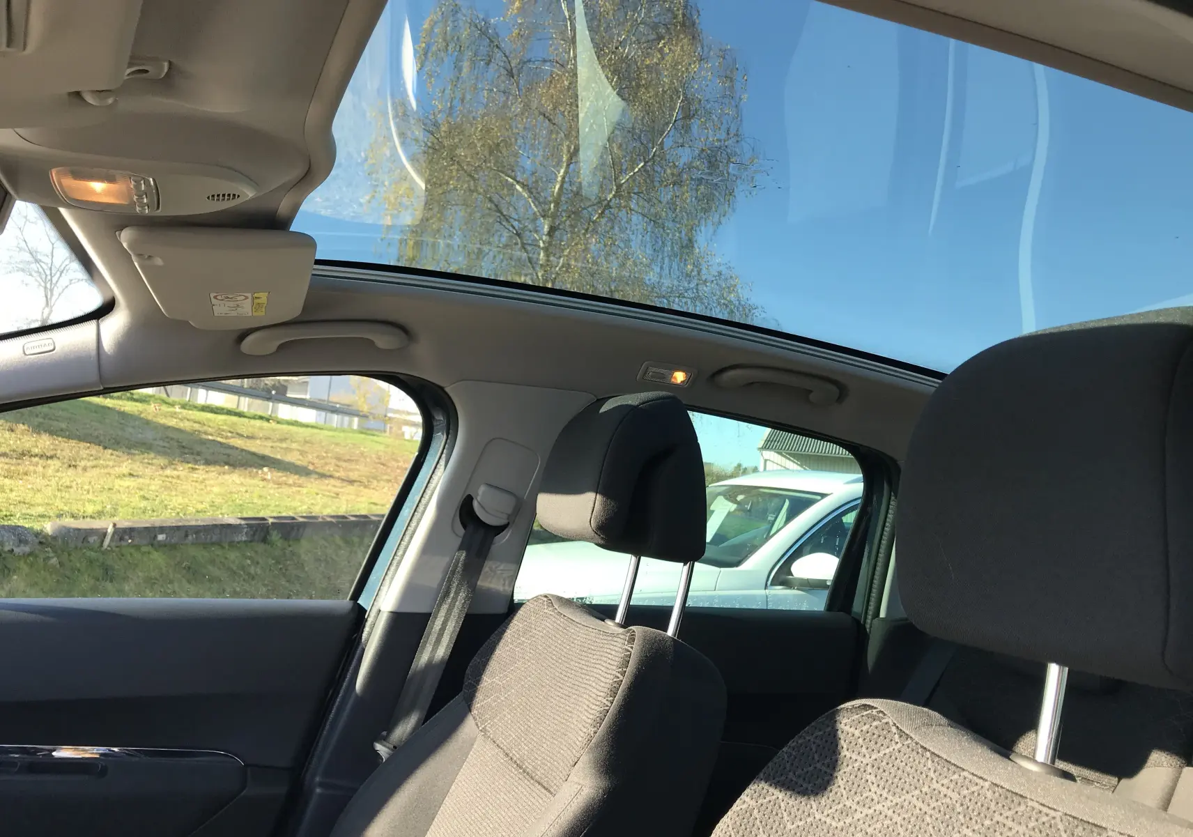 Vue intérieure du Peugeot 3008 Business 2015 montrant les sièges noirs et le toit panoramique sous un ciel bleu clair.