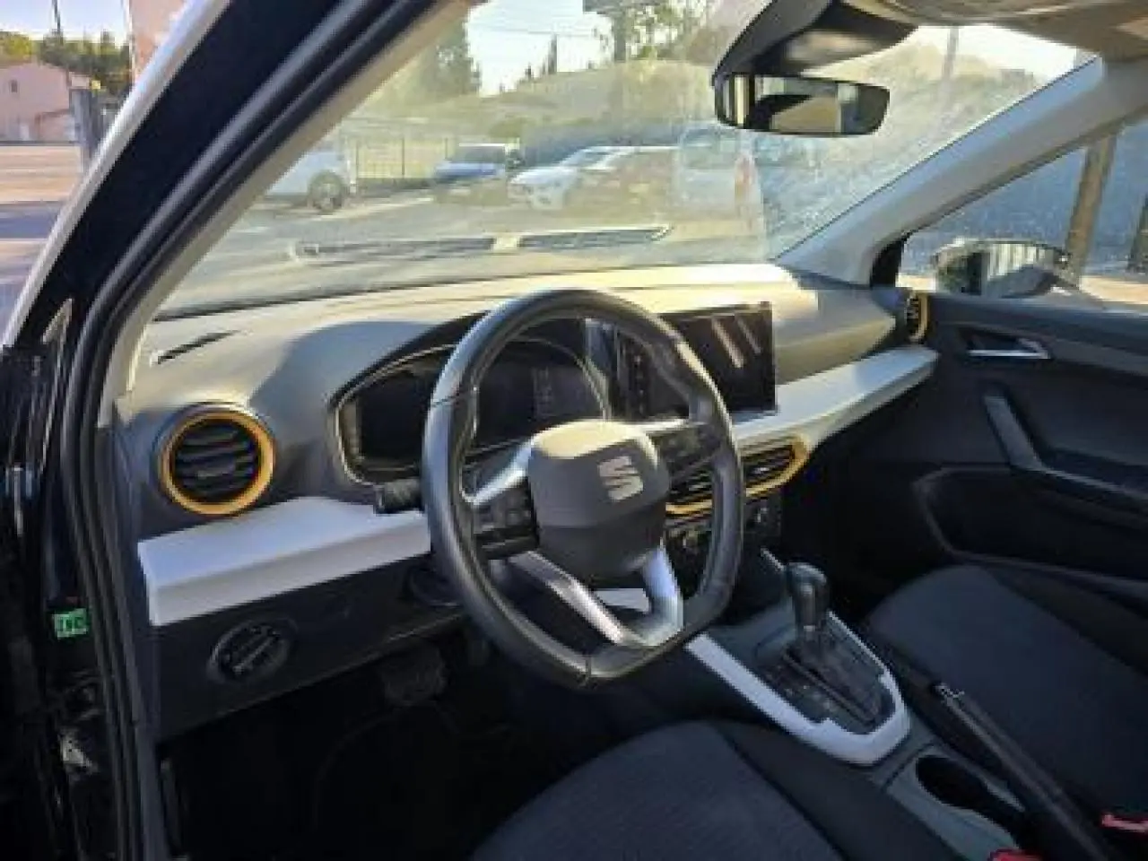 Intérieur du SEAT Arona 2024 vu côté conducteur, volant cuir multifonction et tableau de bord clair avec touches jaunes.