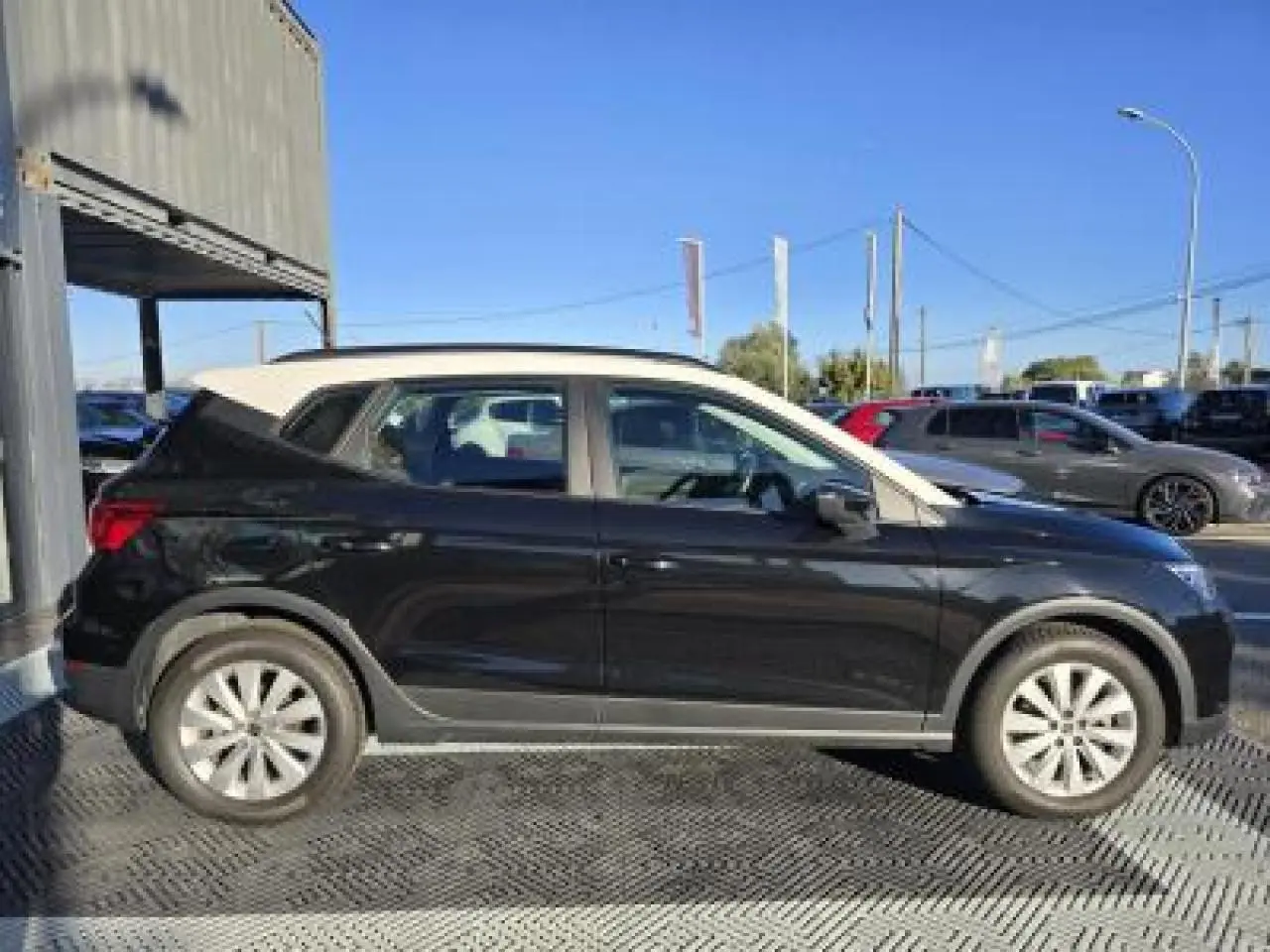 Profil côté gauche d'une SEAT Arona 2024 noir minuit avec toit blanc contrasté, stationnée en extérieur sous un ciel bleu.