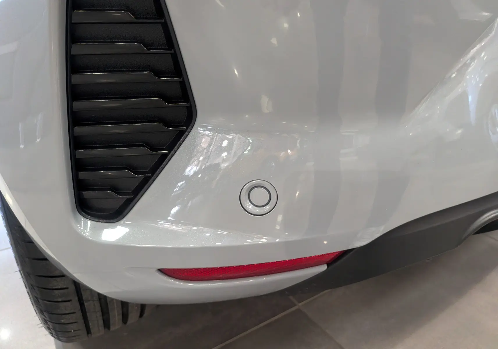 Gros plan sur le pare-chocs arrière gris Rafale de la Renault Clio V avec capteur de recul et feu rouge intégré.