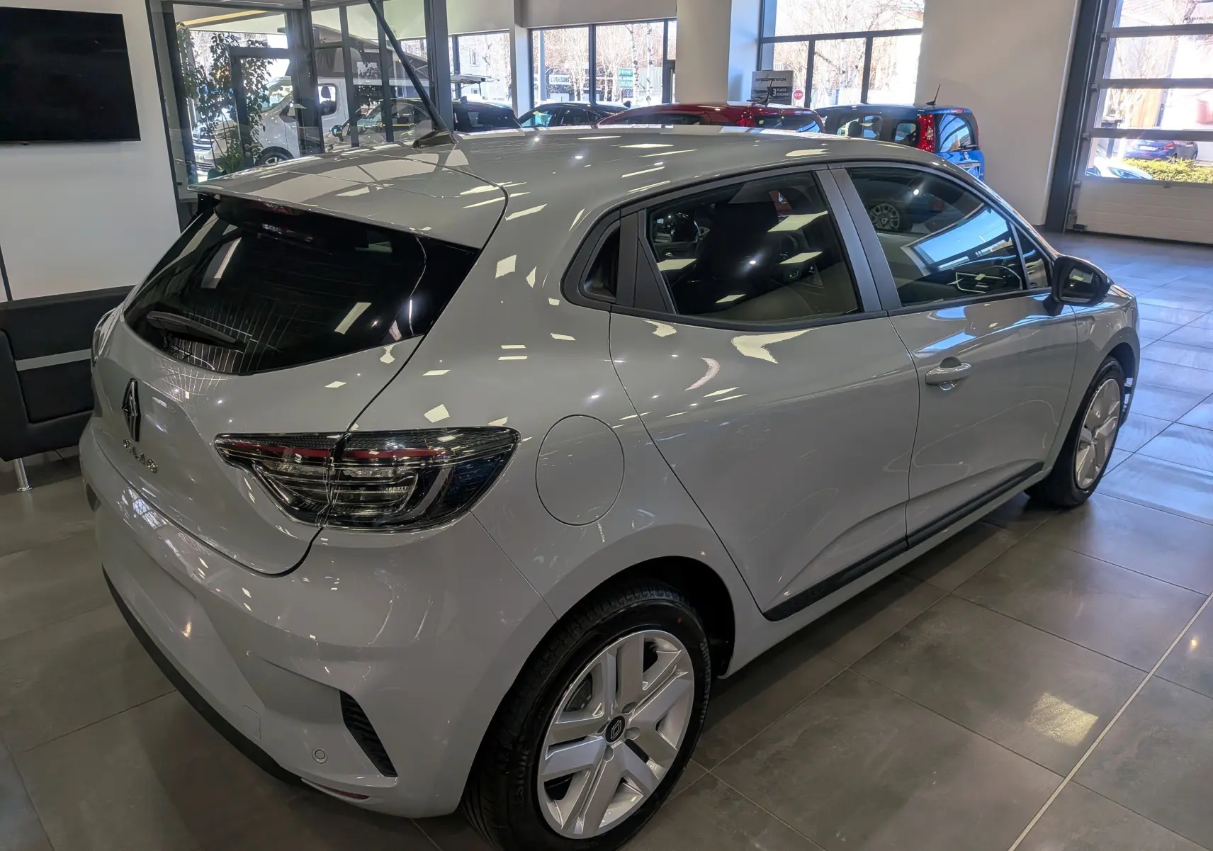 Vue 3/4 arrière droite d'une Renault Clio V gris Rafale en showroom, mettant en valeur ses feux arrière et jantes.
