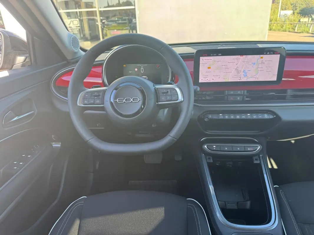 Vue intérieure frontale du tableau de bord de la FIAT 600 rouge 2025, avec volant marqué "600" et écran tactile GPS.