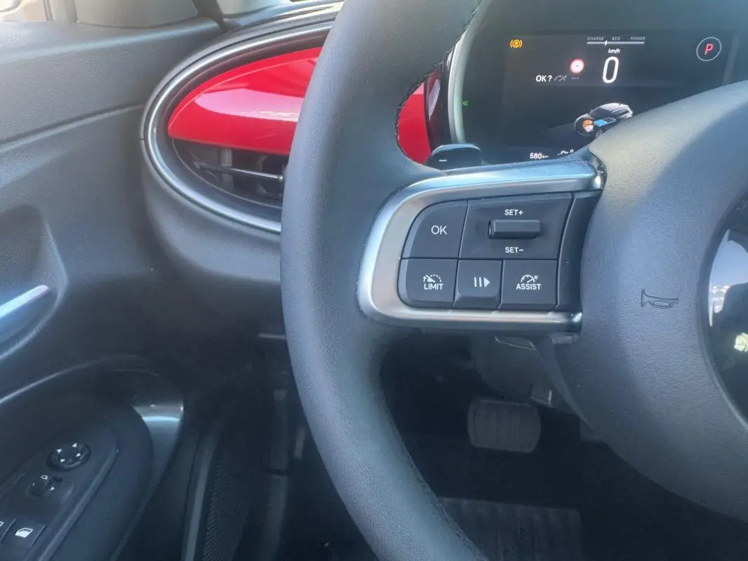Vue intérieure rapprochée du volant et tableau de bord d’une FIAT 600 rouge, avec commandes au volant visibles côté gauche.
