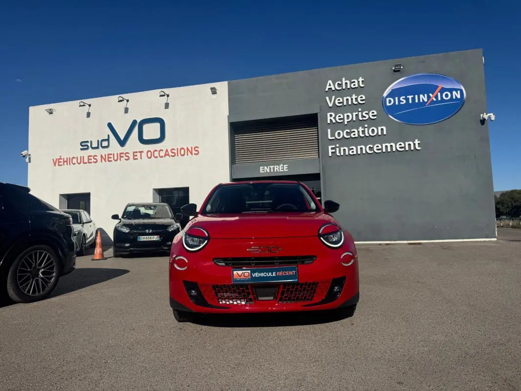 Vue frontale d'une FIAT 600 T-Gen 3 rouge, avec ses phares ronds caractéristiques, stationnée devant un bâtiment commercial.