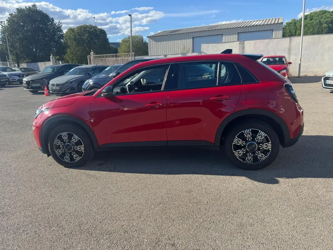 Vue de profil côté gauche d'une FIAT 600 T-Gen 3 rouge 2025 avec jantes au design moderne sur un parking extérieur.