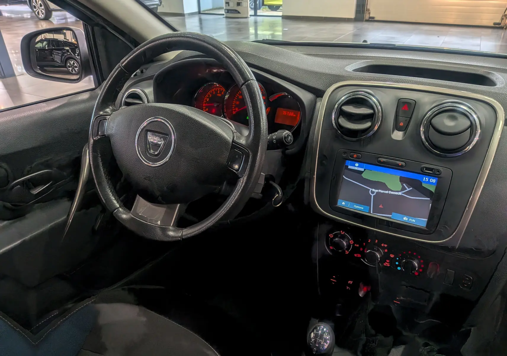 Vue intérieure côté conducteur de la Dacia Sandero TCe 90 blanche avec tableau de bord et écran GPS intégré.