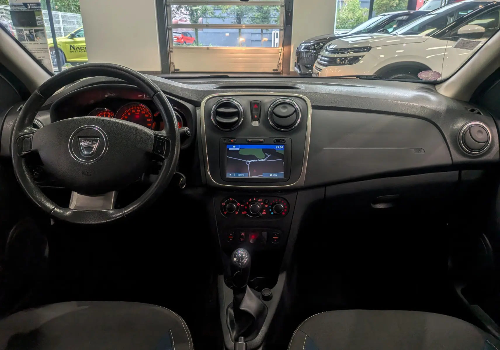 Intérieur de la Dacia Sandero TCe 90 2015 en vue frontale, tableau de bord noir avec écran GPS et volant cuir.