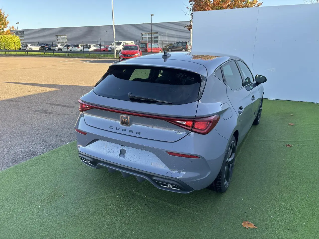 Vue 3/4 arrière droite d'une CUPRA Leon 2024 gris Graphene avec feux arrière LED et double sortie d'échappement.