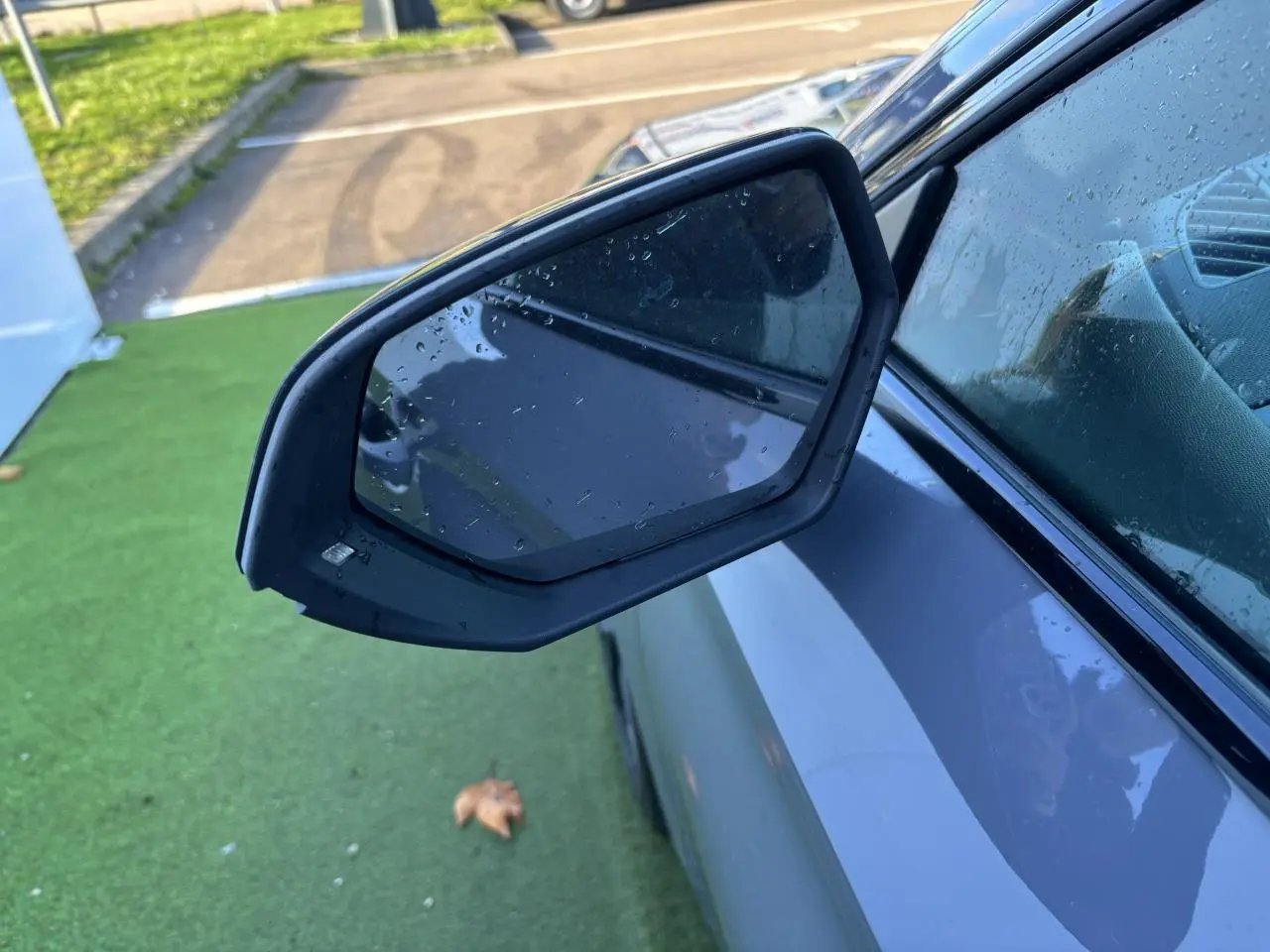 Gros plan sur le rétroviseur côté gauche d'une CUPRA Leon 2024 gris Graphene avec gouttes d'eau visibles.