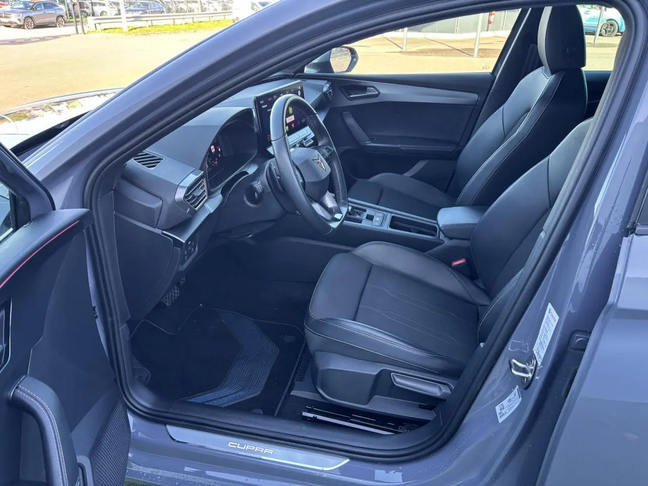 Vue intérieure côté conducteur de la CUPRA Leon 2024 gris Graphene, avec sièges noirs et tableau de bord digital.