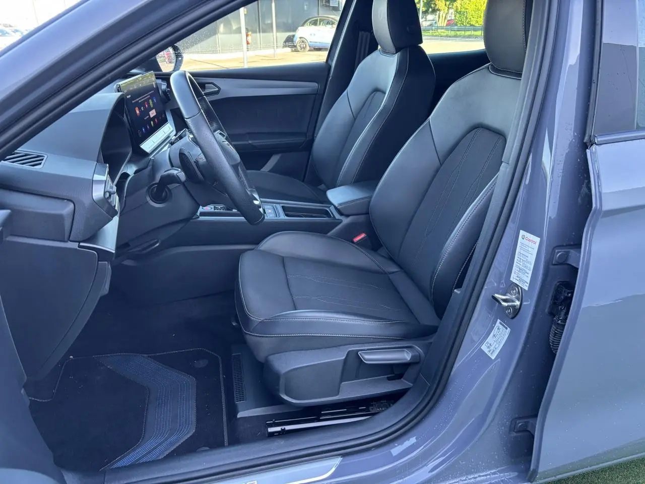 Vue côté conducteur de l'intérieur gris graphene du CUPRA Leon 2024, avec sièges en cuir et écran tactile central.