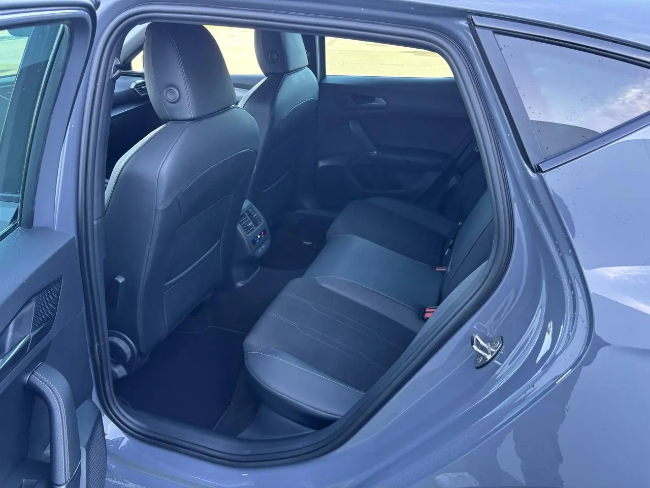 Vue côté arrière gauche de l'habitacle d'une CUPRA Leon gris Graphene, montrant les sièges arrière en cuir noir et les commandes de climatisation.