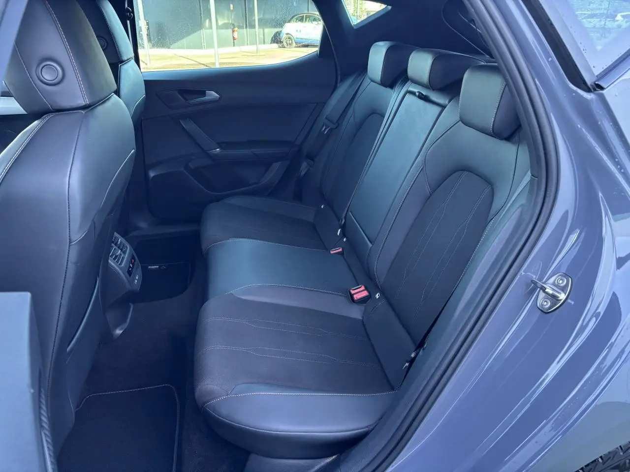 Vue intérieure côté droit des sièges arrière en cuir noir du CUPRA Leon 2024 gris Graphene, avec ceinture rouge visible.