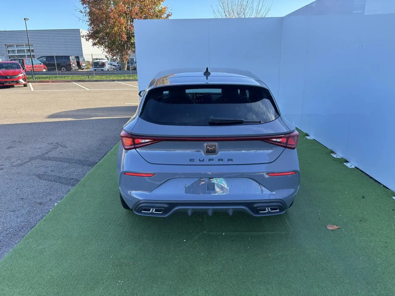 Vue arrière d'une CUPRA Leon 2024 gris Graphene avec feux LED reliés par un bandeau lumineux et double sortie d'échappement.